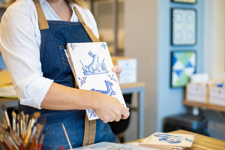 An artisan holding blue and white ceramic tiles in a well-lit workshop, showcasing traditional craftsmanship.
