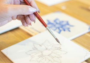 Close-up of hand painting a ceramic tile with floral design in a Portuguese workshop.
